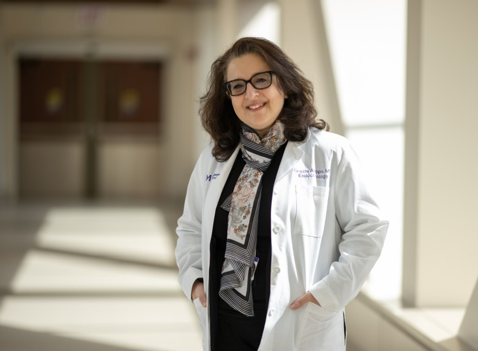Photo of Dr. Grazia Aleppo standing in naturally-lit hallway with her hands in her white coat pockets